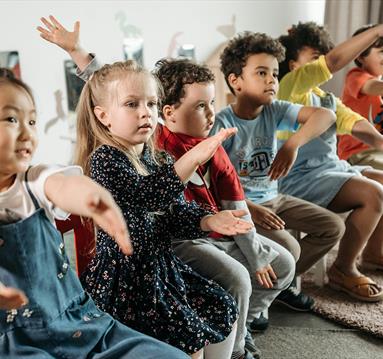 Photo of children sitting in a line of chairs.