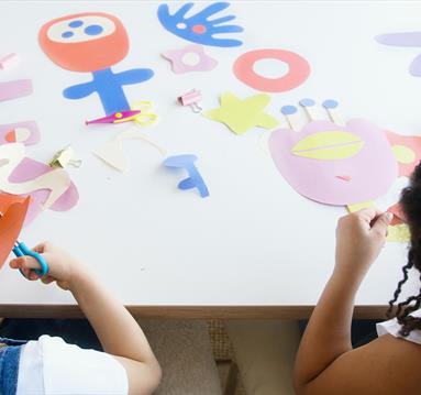 Two children cut out colourful pieces of card