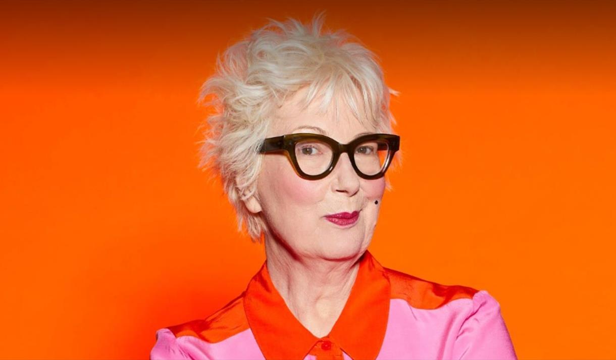 Photo of Jenny Eclair in front of a vibrant orange background