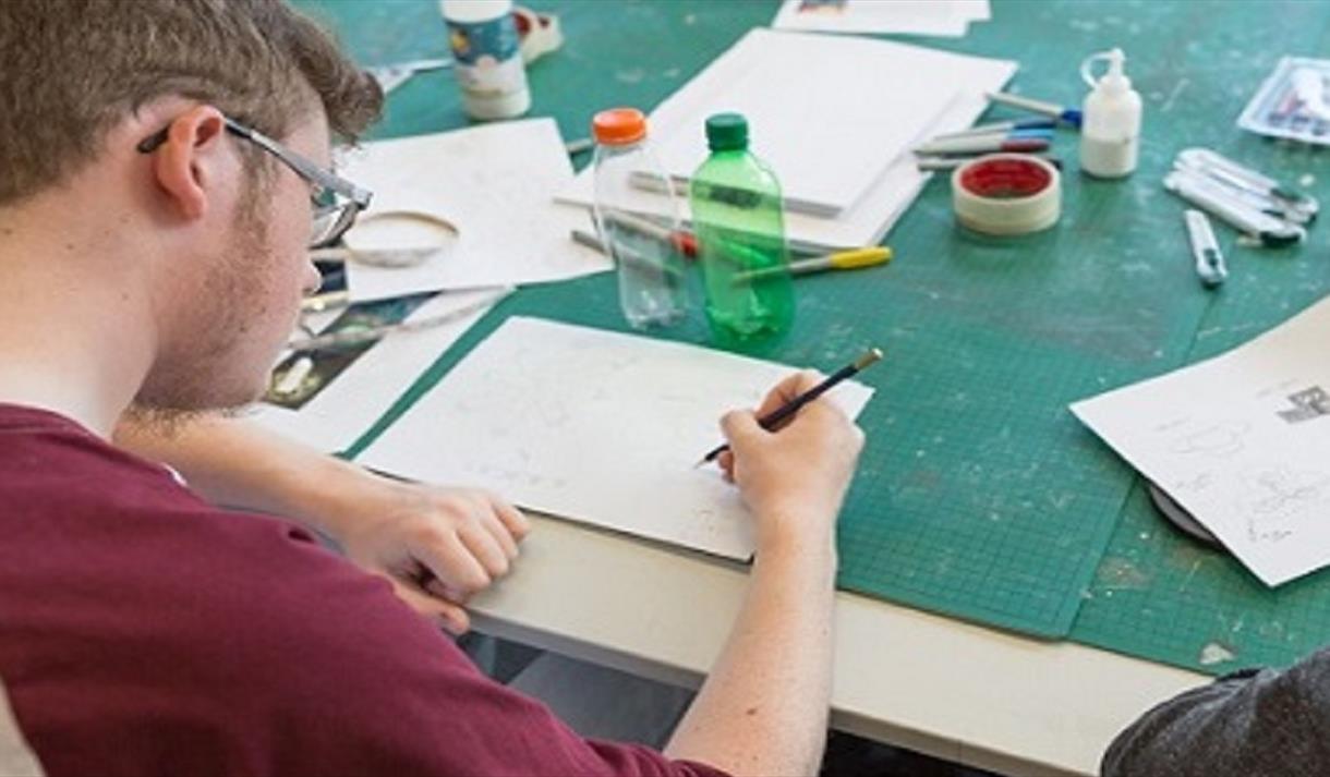 Photo of a student writing in a notebook, taken from behind his shoulder.