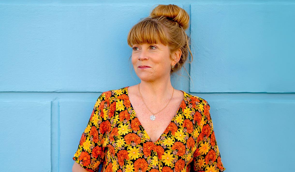 Sara Oschlag stood infront of a blue wall wearing a floral top