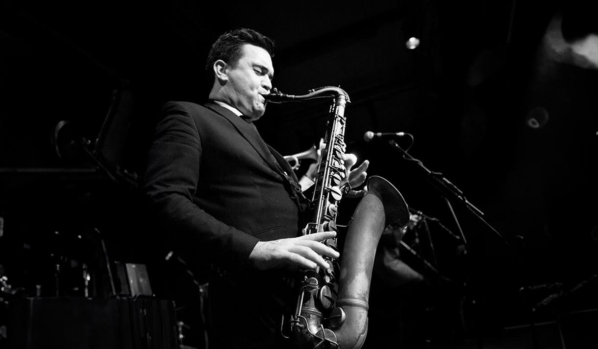 Black and white photo of a member of the Brandon Allen Quartet playing a saxaphone mid-performance