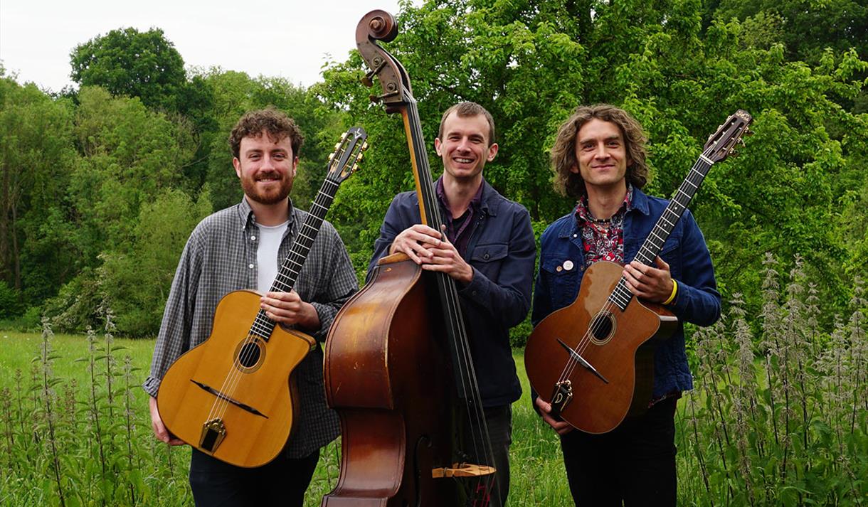 Photo of the Trio holding their instruments, standing in a field