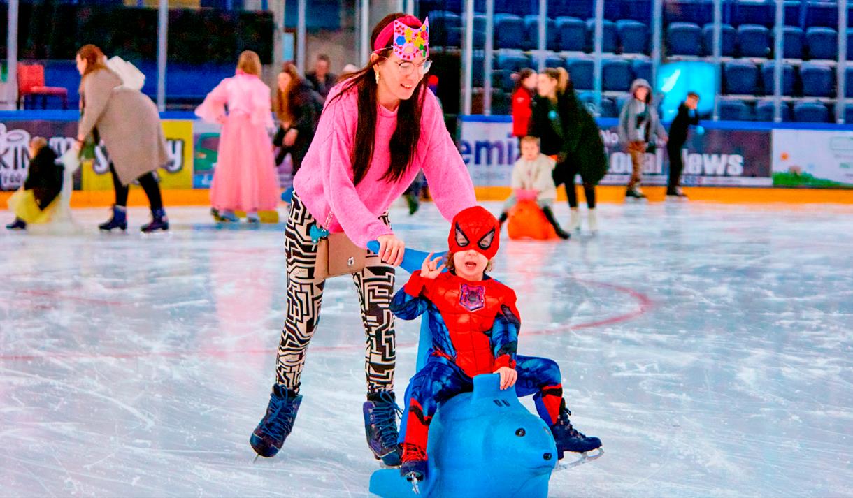 Photo of a mum and young son dressed as spiderman enjoying an ice-skating session using ice equipment.