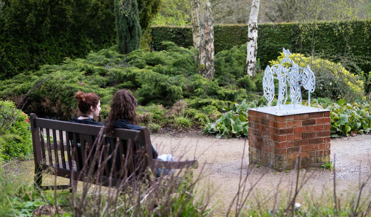 Photo of one of the art installations. Two people are sitting on a bench opposite, looking at it.