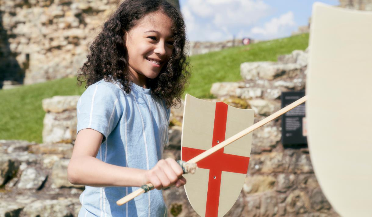 A young child stands holding a wooden sword and St. Georges Cross shield