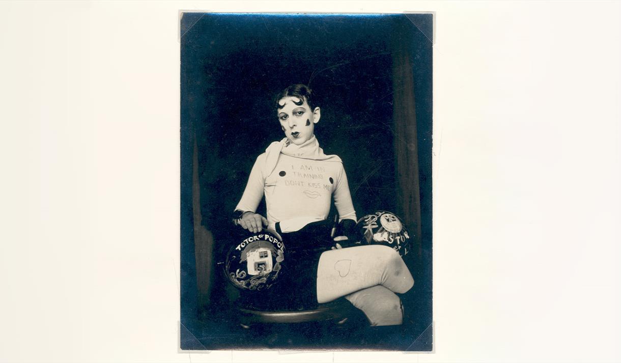 Portrait by Claude Cahun of a lady sat on a chair cross legged.