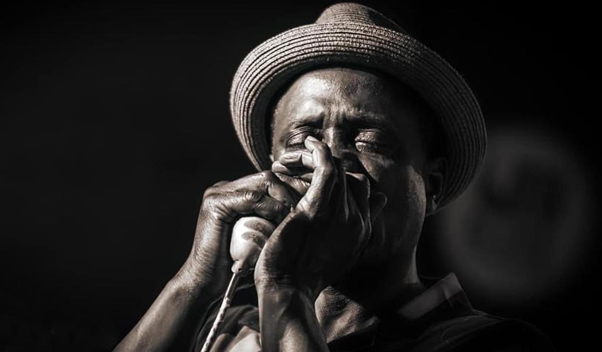 Black and white photo of a performer playing a harmonica into a microphone