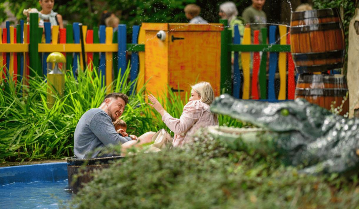 Photo og a family on a water ride, with a toy aligator int he foreground and colourful fences in the background. They are laughing and happy.