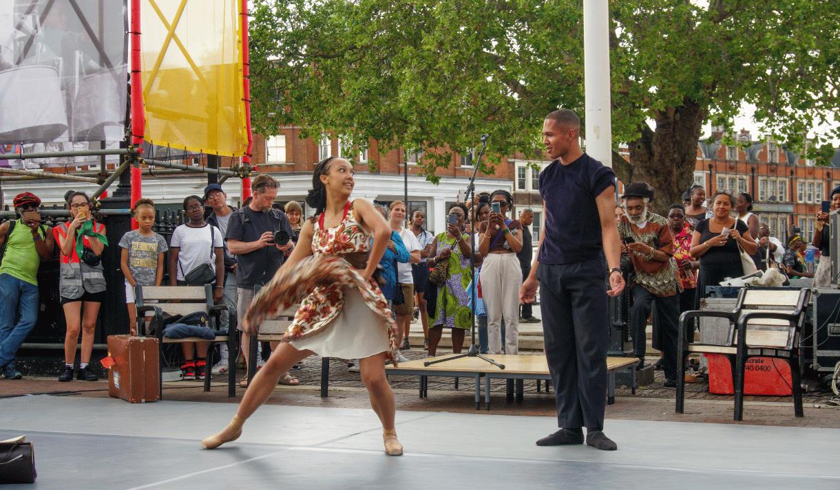 Photo of two dancers on an outdoor stage with a crowd visible behind them