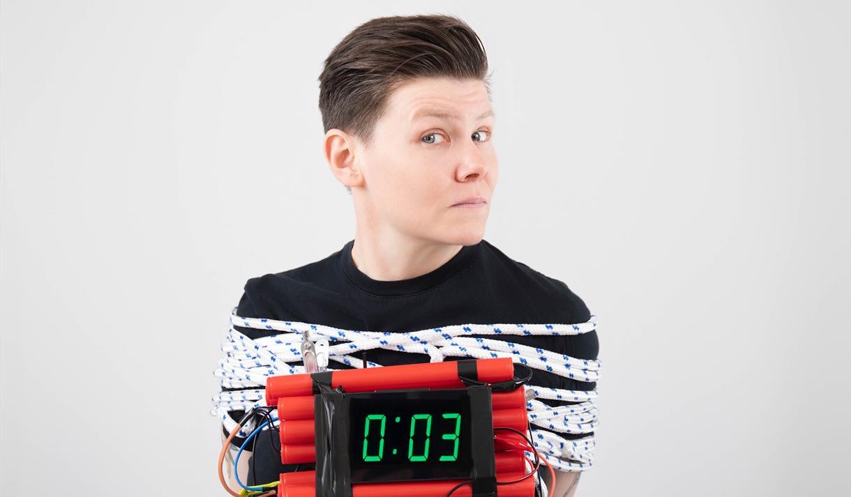 Image of Grace Petrie bound by ropes and holding a bomb that only has 3 seconds before it will detonate.