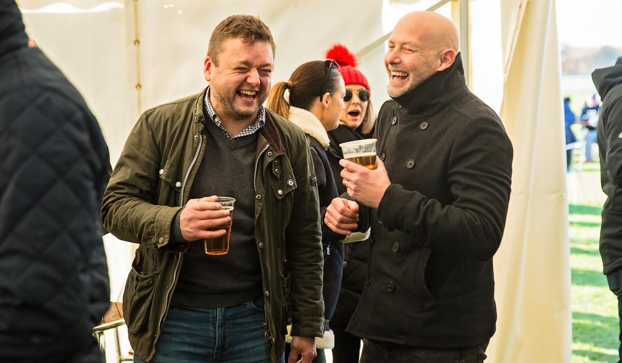 Photo of two men in a better trent, pints in hand, laughing and smiling.