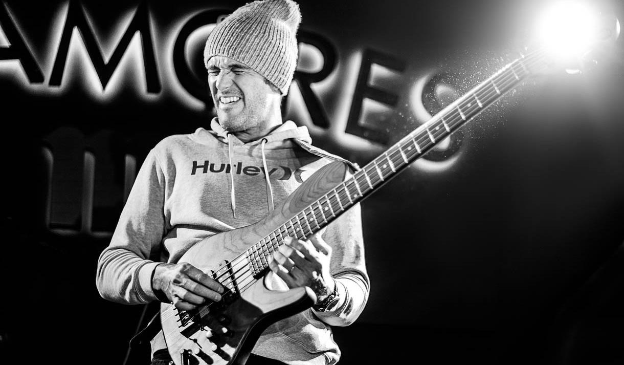 Black and white photo of one of the guitarists for the trio playing on stage at another performance.