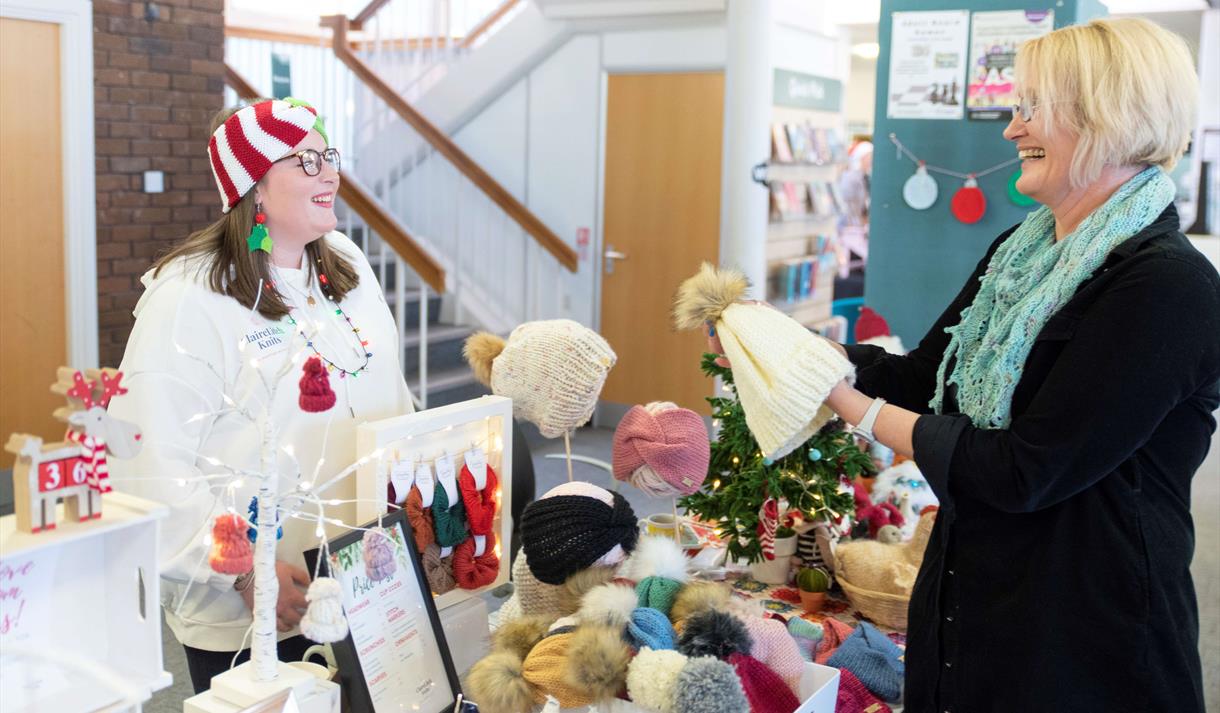 A stallholder selling knitted items smiles as she talks to a customer