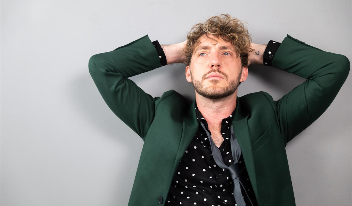 Comedian Seann Walsh, wearing a spotted shirt, black tie and dark green jacket