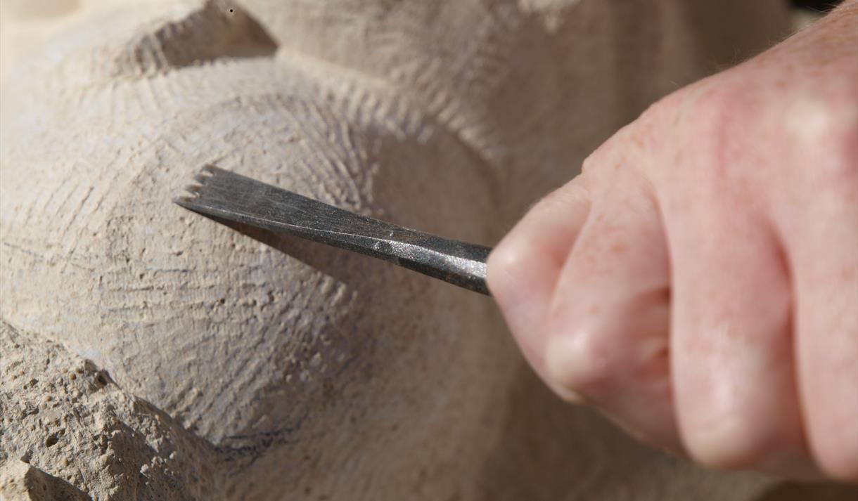 Image shows a mans hand carving a stone