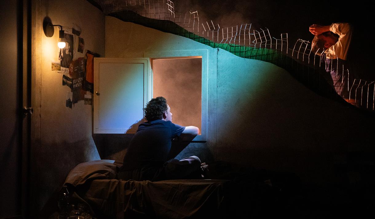 Image shows a young boy sitting alone in a dark room with an open door and a blue light shining in.