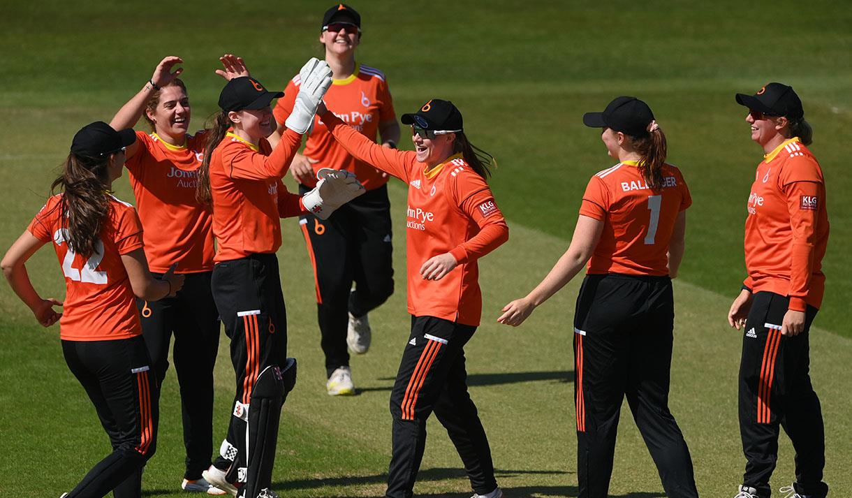 A photo of the women's cricket team ont he pitch. They are hi-5ing one another.