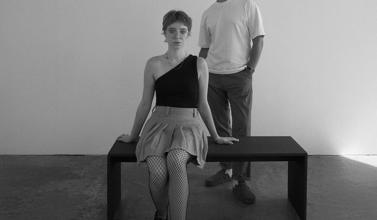 Image of a lady sat on a bench with a young man stood behind.
