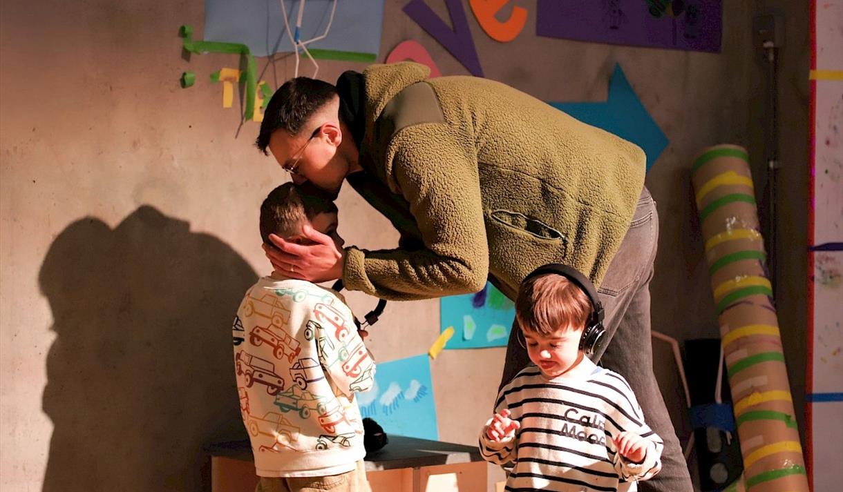 A father beding down to kiss his child, who is engaged in a play session