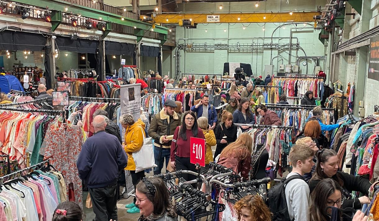 Crowds gathered around rails of discounted clothing at an indoor flea market