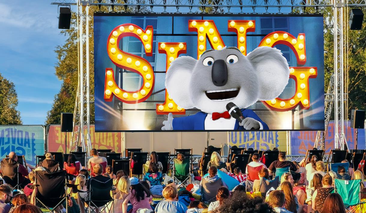 Photo of an outdoor cinema screen showing a still from SING.