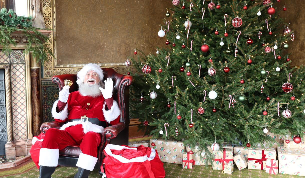 Photo of a jolly Santa sitting in a leather armchair, next to a Christmas tree