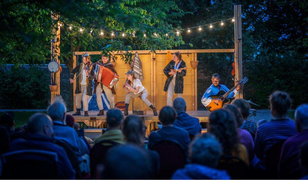 Photo of an outdoor theatre in the evening with performers lit up on stage