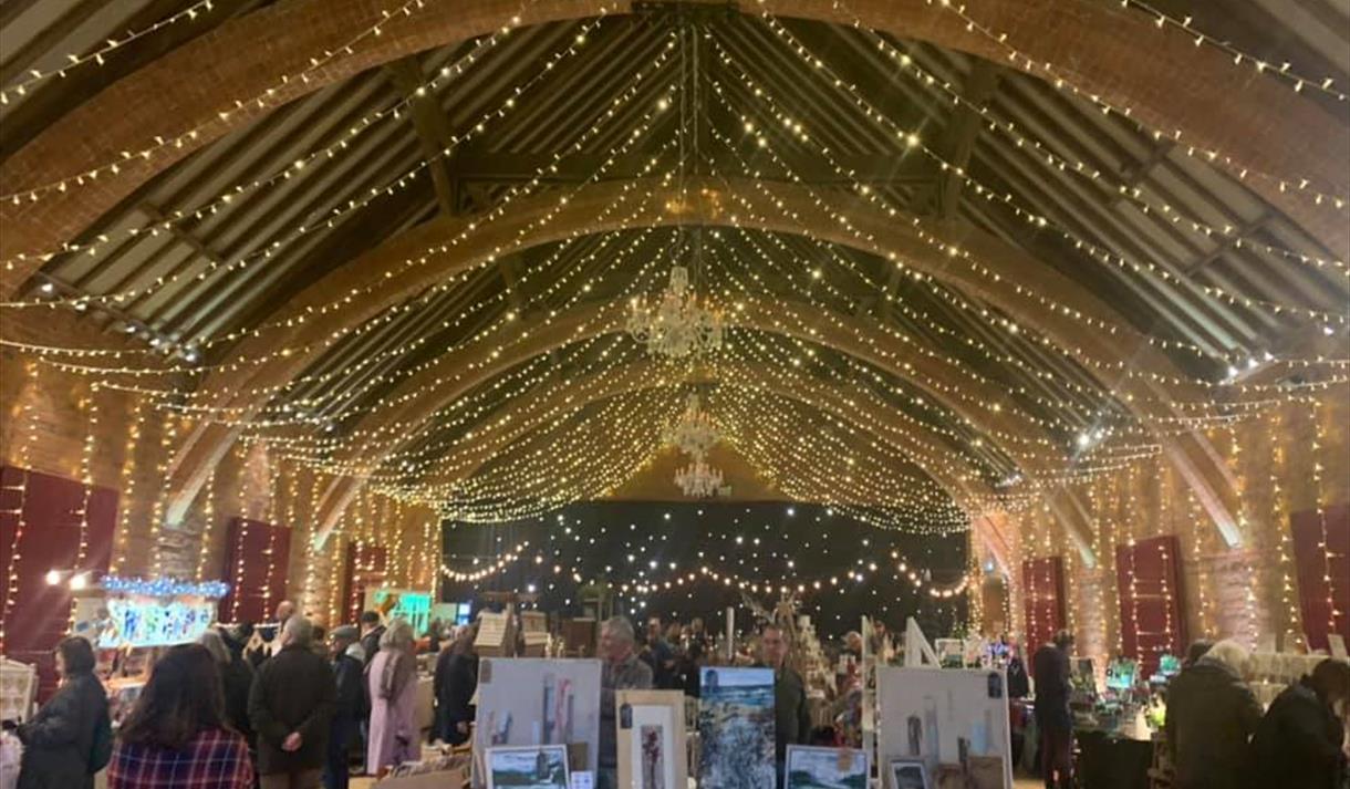 An indoor hall adorned with string lights for a warm and cosy atmosphere.You can see tables laid in the shape of market stalls, with arts and crafts f