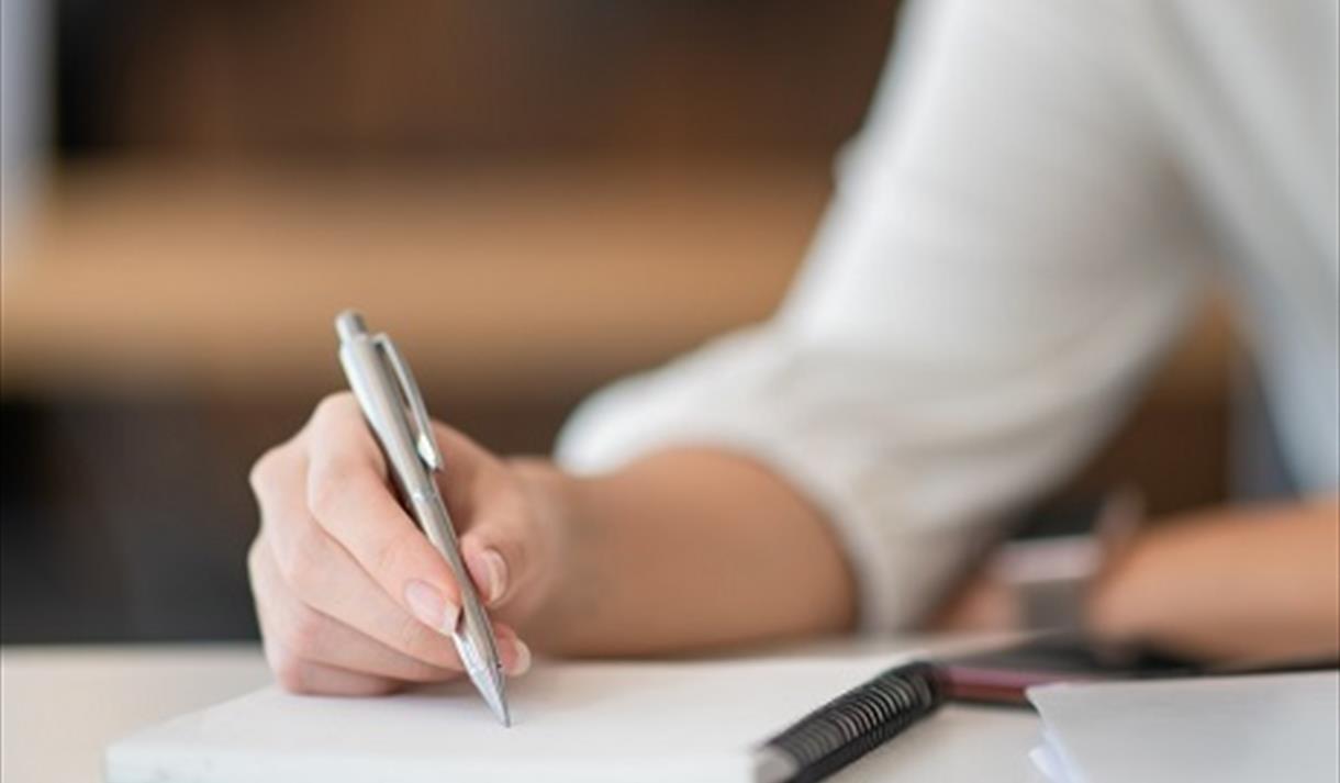 Image shows a hand writing on a notepad