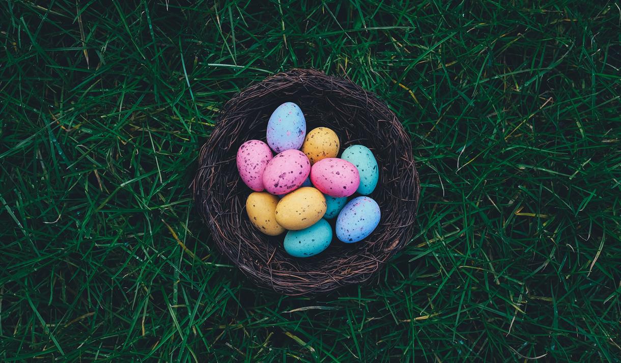 Photo of colourful easter eggs in a wicker basket.