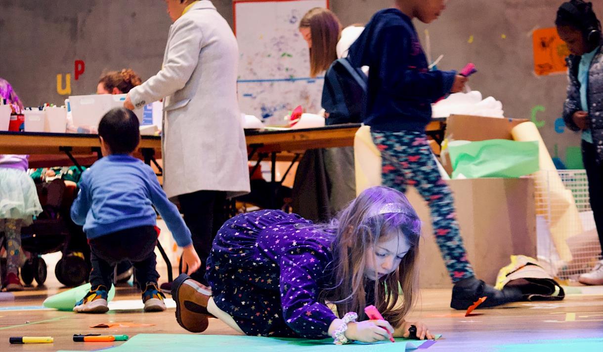 Photo of children at Nottingham Contemporary. A young girl is seen in the foreground colouring on the floor