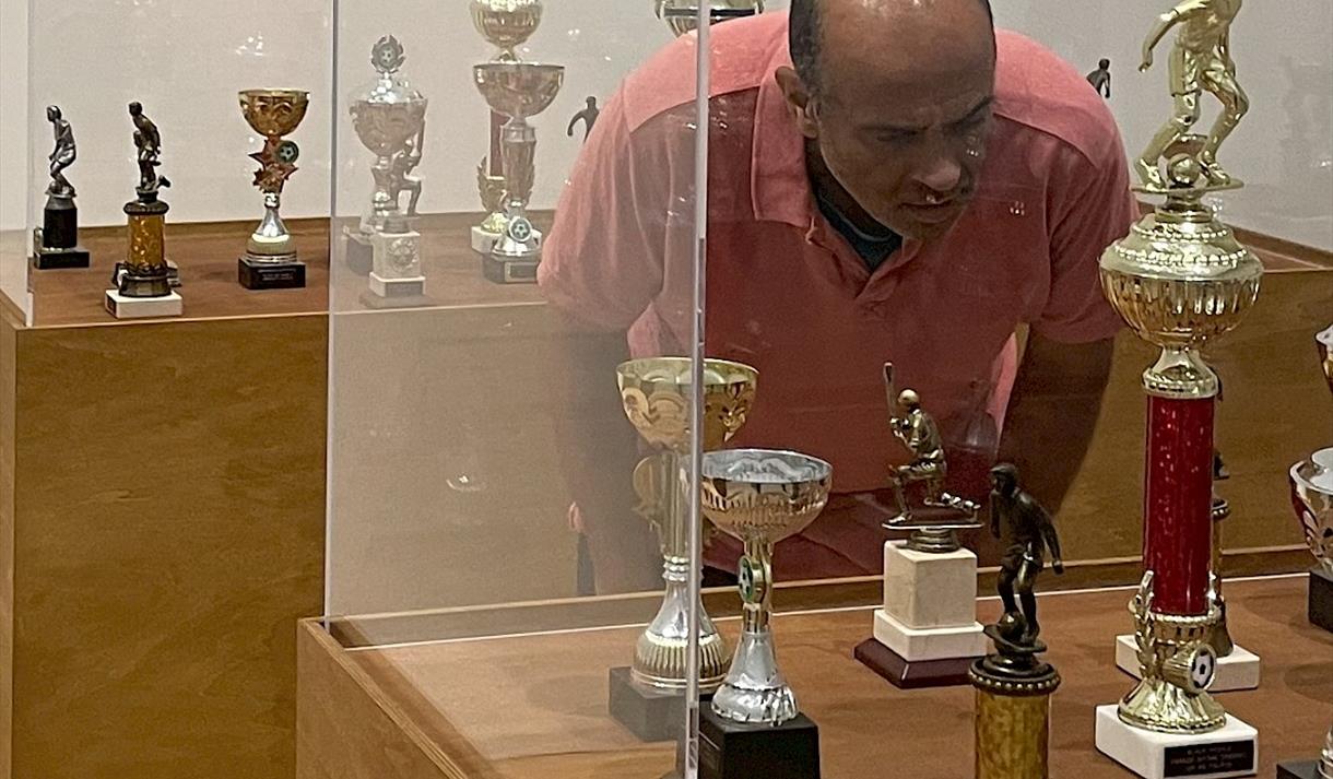 Photo of a man looking at trophies behind a glass exhibition