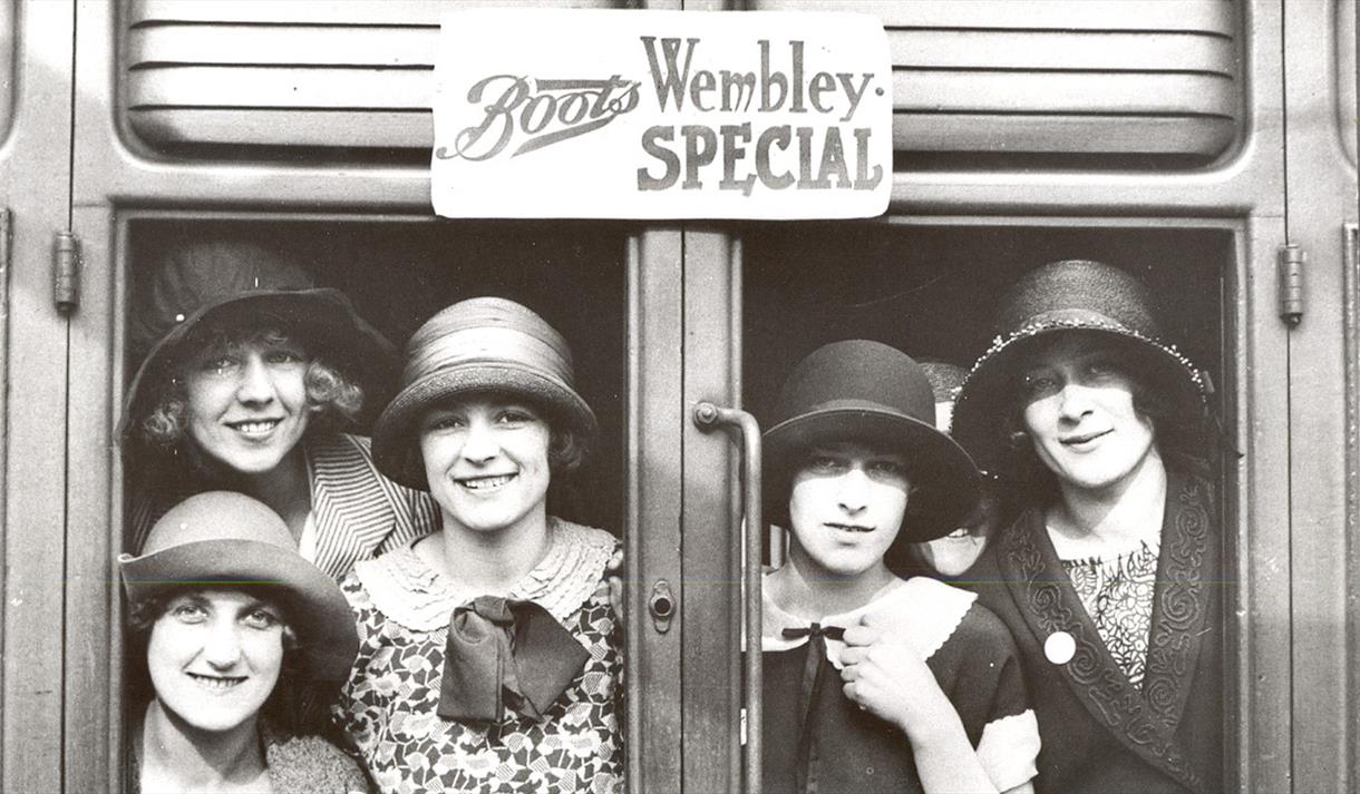 Old black and white photo of a group of women, taken through a set of glass doors, presumably at a Boots storefront.