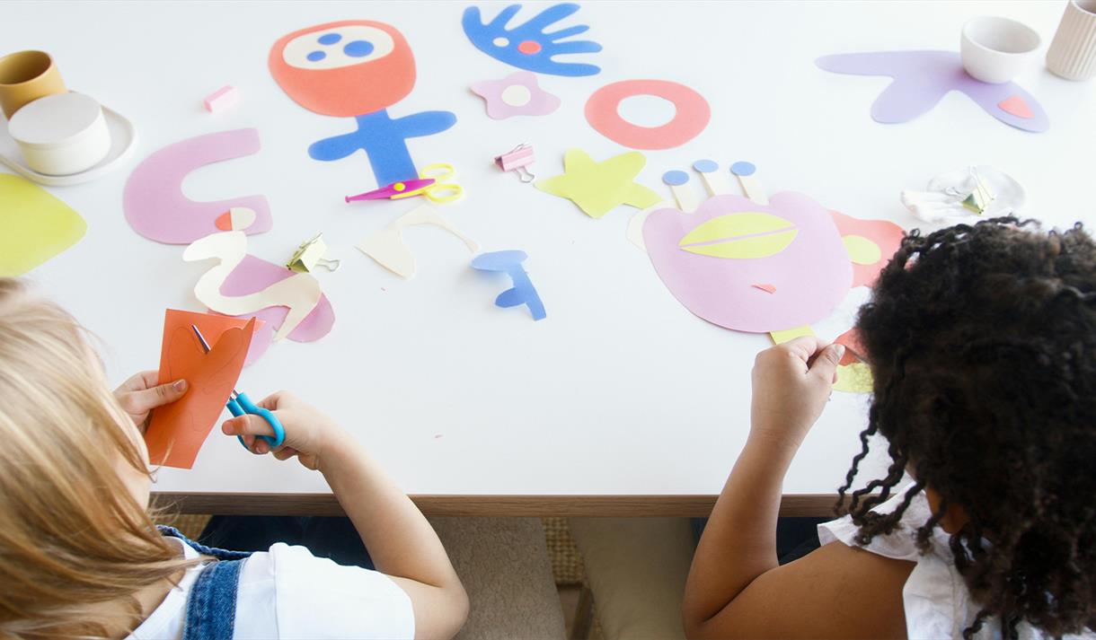 Two children cut out colourful pieces of card