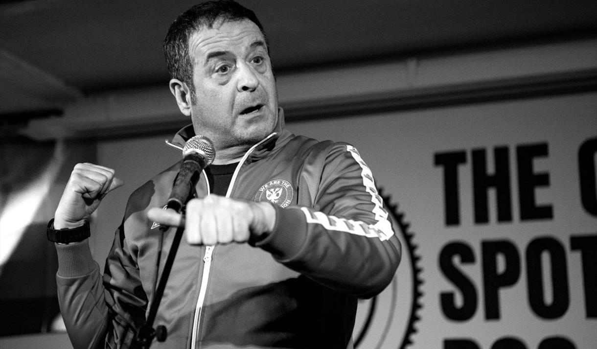 Image shows a black and white image of Mark Thomas on stage during his show - Gaffa Tapes.