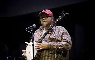 Riley Baugus speaks, banjo in hand, to the audience between numbers