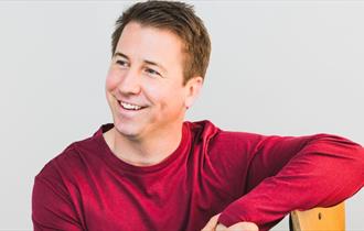 Photograph of Carl Hutchinson wearing red sweater, grey background