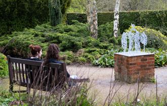 Photo of one of the art installations. Two people are sitting on a bench opposite, looking at it.