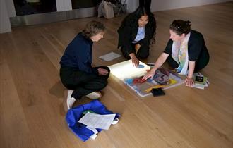 Three people seated on the floor around an art sketchbook