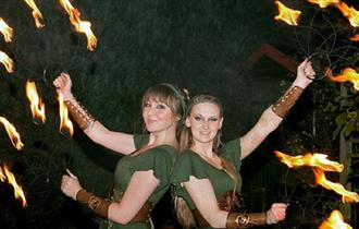 Two women in Robin Hood costumes juggling with fire