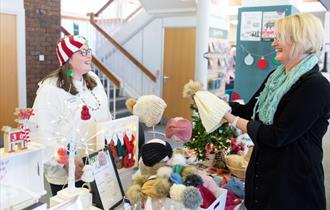 A stallholder selling knitted items smiles as she talks to a customer