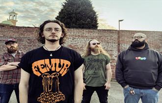 Four band members stand in front of a brick wall