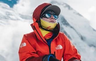 Mountaineer Adriana Brownlee pictured wearing an orange hiking jacket in front of a snow-covered mountain