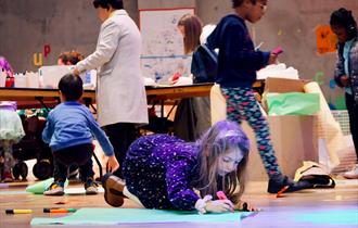 Photo of children at Nottingham Contemporary. A young girl is seen in the foreground colouring on the floor