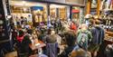 A crowd gahers in a pub. Some are sitting, some are having to stand at the back.