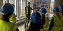 Students wearing hard hats and hi-vis jackets observing a presentation from a construction worker.