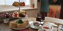 A serving of Afternoon Tea for two. A three tier cake stand showcasing sandwich squares, a mixture of cakes and fruit scones. Two teacups and saucers