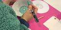 Photo of a person in an arts and crafts session. They are holding a bowl and a paint pen. The photo is taken from behind their right shoulder.