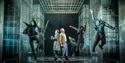 Minority Report - Two people stand back to back in the middle of a white circle on the floor, looking scared. Around them, people in grey clothes leap